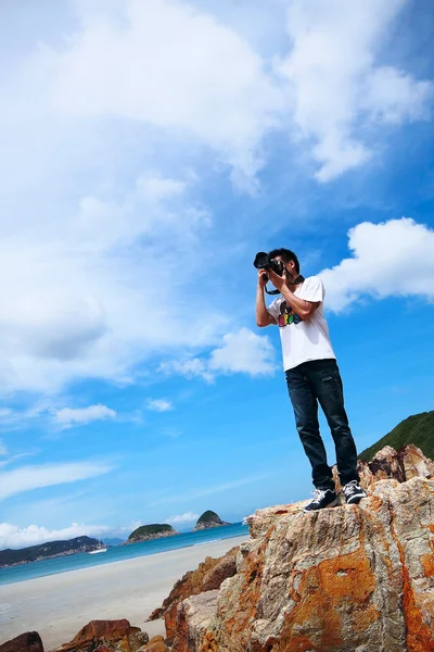 Πορτρέτο ενός νεαρού άνδρα που στέκεται σε μια παραλία με μια φωτογραφική μηχανή — Φωτογραφία Αρχείου
