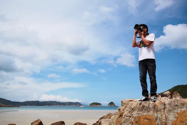 Portrait of a young man standing on a beach with a camera — Stock Photo, Image