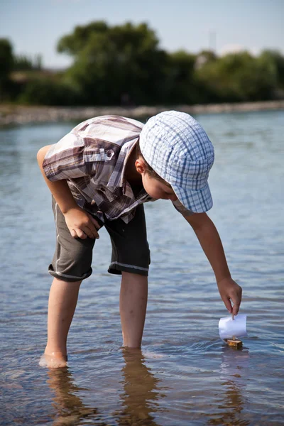 Pojke lanserar en liten segelbåt i floden — Stockfoto