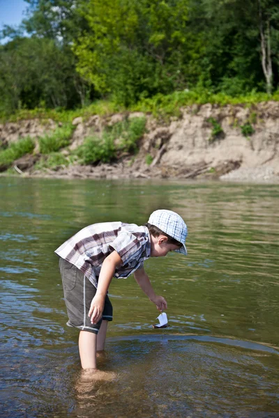 Pojke lanserar en båt i floden Stockbild