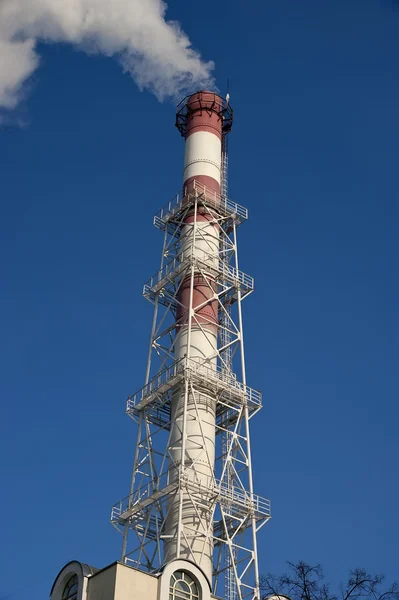 Průmyslové komíny s vlající bílý kouř, který se dostává do atmosféry proti modré obloze — Stock fotografie