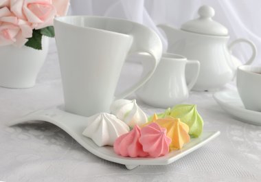 Meringue cookies of different colors on a plate with a cup of co clipart