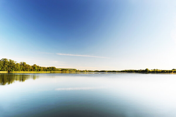 Calm water of lake, woods on other side and blue sky. landscape