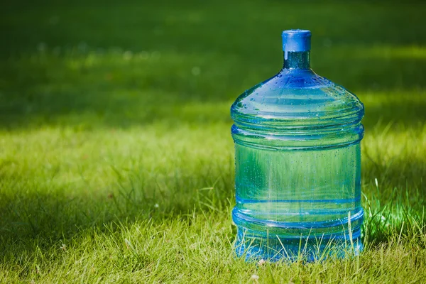 Большая бутылка воды на зеленом фоне травы — стоковое фото