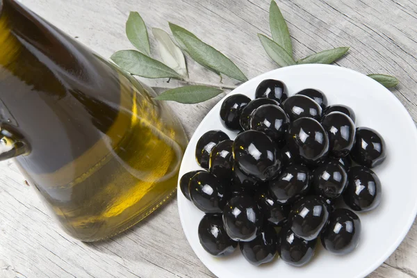 Olio d'oliva e un piatto con olive nere . — Foto Stock