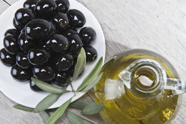 Olive oil and a plate with black olives. — Stock Photo, Image