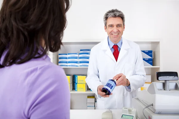 Doctor mostrando un contenedor de pastillas en la farmacia —  Fotos de Stock