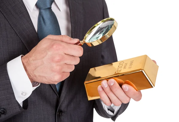 Hombre de negocios mirando la barra de oro a través de la lupa —  Fotos de Stock