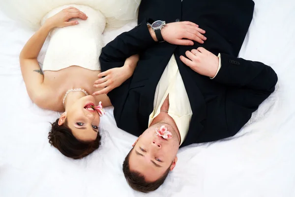 Braut und Bräutigam liegen im Schlafzimmer mit Orchideen — Stockfoto