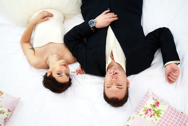 Bride and groom lying in bedroom with orchids — Stock Photo, Image