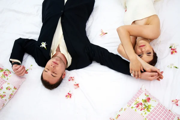 Bruid en bruidegom liggen in slaapkamer met orchideeën — Stockfoto
