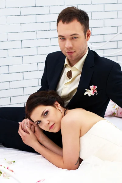 Bride and groom sitting on bed in bedroom — Stock Photo, Image