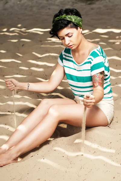 Chica con tatuaje en la playa vierte arena — Foto de Stock