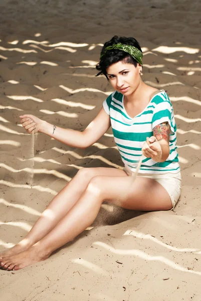 Meisje met een tatoeage op het strand giet zand — Stockfoto