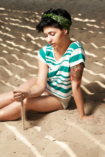 Flicka med tatuering på stranden häller sand — Stockfoto