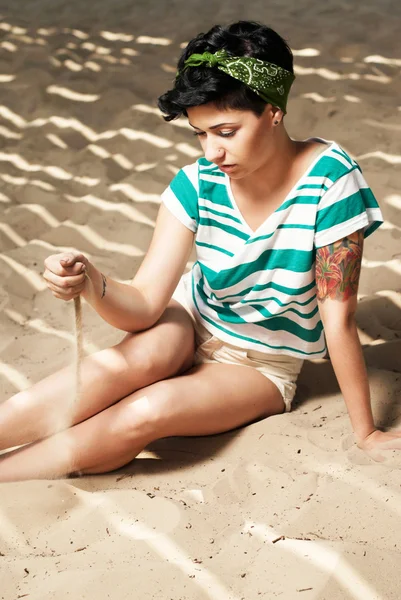 Pige med tatovering på stranden hælder sand - Stock-foto