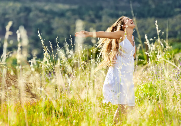 Beautiful girl laughs and dances outdoors in a meadow durning sunset
