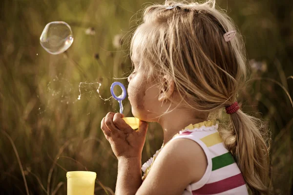 Cute girl blowing bubbles in a field — Stock Photo, Image