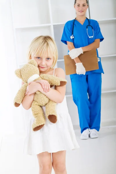 Маленькая девочка держит плюшевого мишку в кабинете врача — стоковое фото