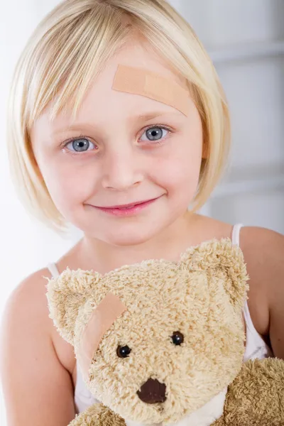 Liten flicka med plåster på hennes ansikte som innehar en nallebjörn — Stockfoto