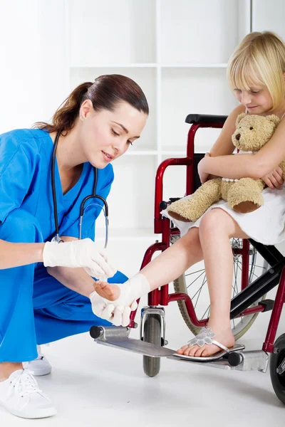 Omtänksam sjuksköterska bandage lilla flickans fotled — Stockfoto