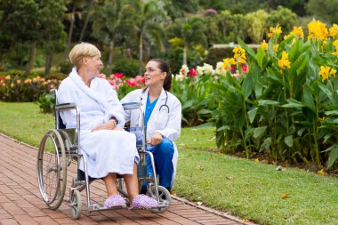 Caring female nurse talking to disabled senior patient clipart