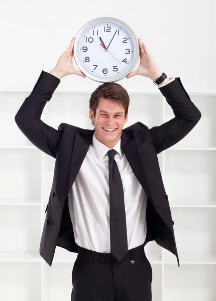 Young businessman holding a clock in office — Stock Photo, Image