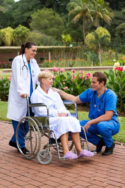 Male doctor talking to senior patient in hospital garden — Stock Photo, Image