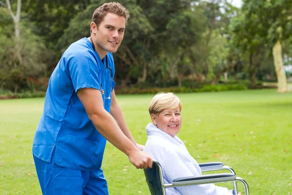 Νοσοκόμος, ωθεί έναν ανώτερο ασθενή σε αναπηρική καρέκλα σε εξωτερικούς χώρους — Φωτογραφία Αρχείου