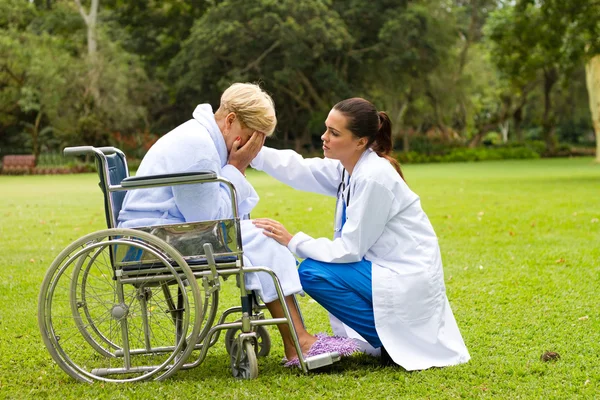 Giovane medico confortante un paziente anziano disabile solitario all'aperto — Foto Stock