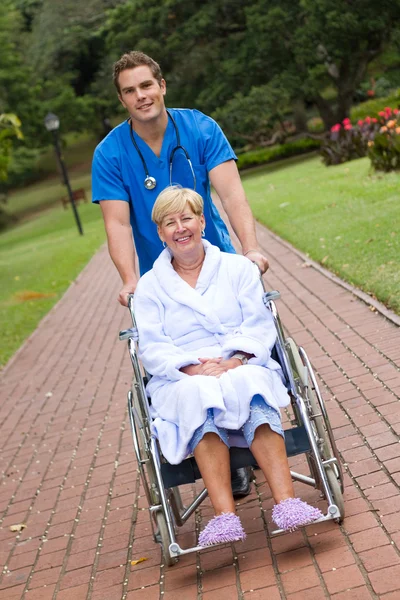 Male medical nurse pushing senior patient on wheelchair outdoors Royalty Free Stock Images
