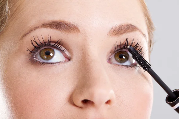 Young woman applying mascara on her eyelashes — Stock Photo, Image
