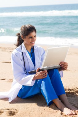 Young female doctor working on laptop on beach clipart