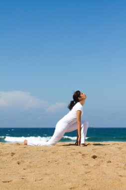 Kumsalda yoga yaparken sağlıklı genç bir kadın
