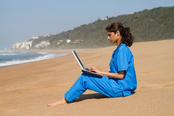 Νεαρή γυναίκα γιατρό χρησιμοποιώντας φορητό υπολογιστή στην παραλία — Φωτογραφία Αρχείου