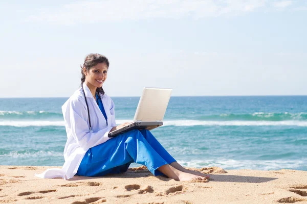 Kumsalda dizüstü bilgisayarda çalışan genç bir kadın doktor — Stok fotoğraf