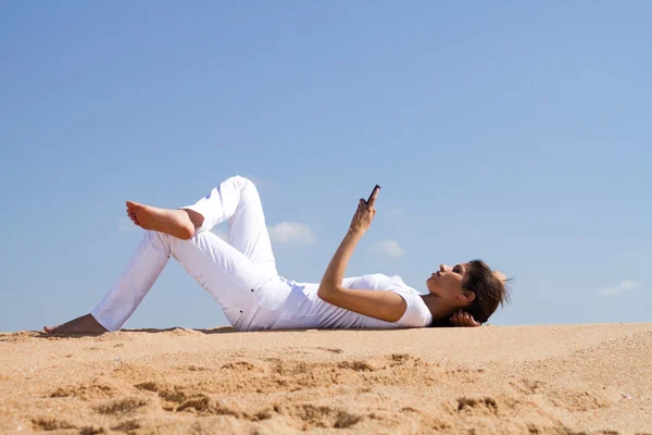 Junge Frau liegt am Strand und liest SMS vom Handy — Stockfoto