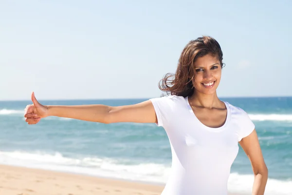 Молодая женщина подает большие пальцы вверх руку знак на пляже — стоковое фото