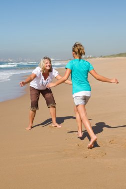 Teen daughter running to mother on beach clipart