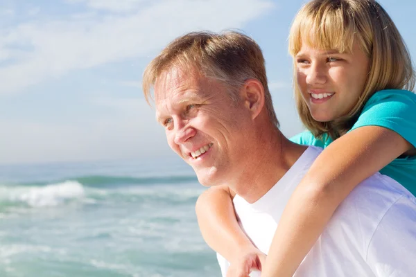 Отец катается на спине к дочери на пляже — стоковое фото