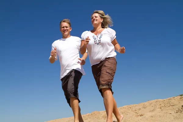 Medelålders par som springer på stranden — Stockfoto