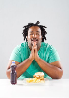 Overweight african american man pray before eating a meal clipart