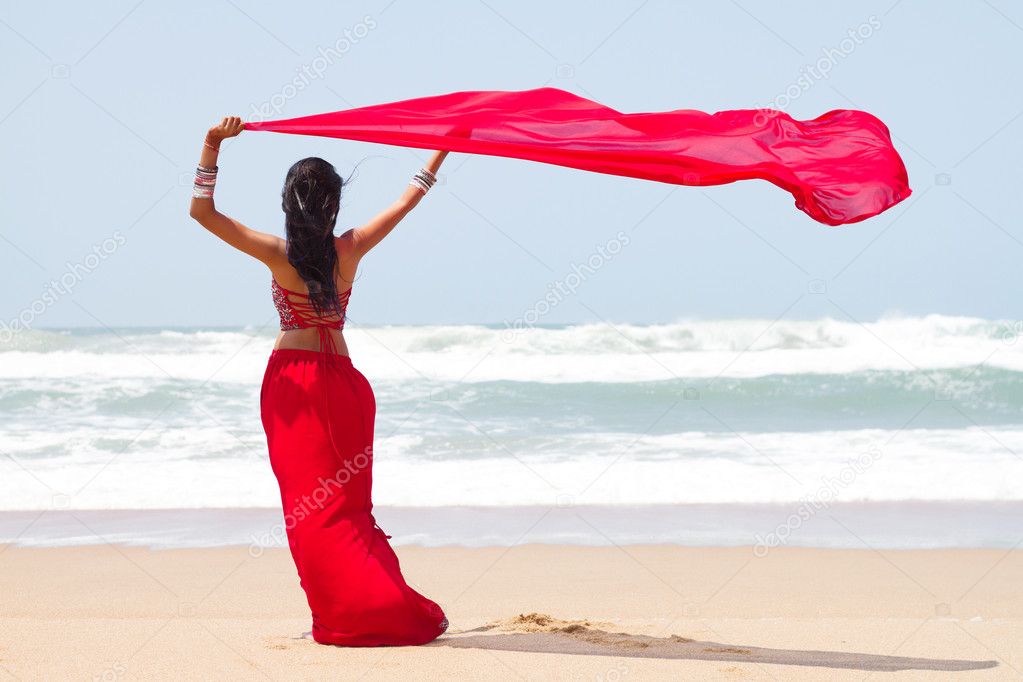 Young woman holding a sarong on windy beach
