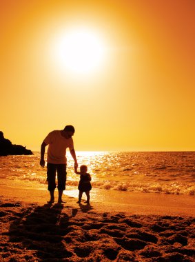 Father and daughter playing on the beach at sunset clipart