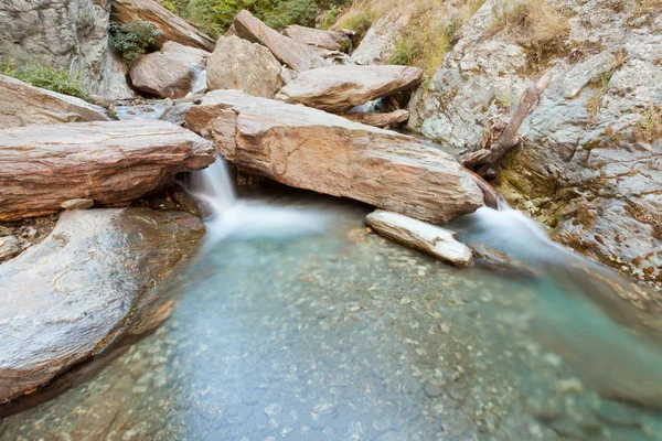 Small waterfall casdcading over rocks in blue pond — Stock Photo, Image