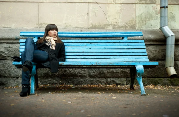 Mladá žena v černém kabátě, sedí na lavičce — Stock fotografie
