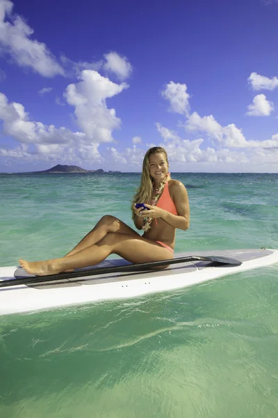 Jovem mulher de biquíni em paddle board mensagens de texto — Fotografia de Stock