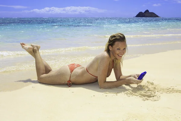Menina loira bonita em biquíni mensagens de texto na praia — Fotografia de Stock