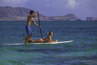 Couple on standup paddle board in hawaii clipart