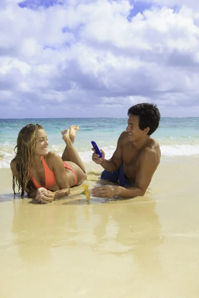 Couple on the beach in hawaii with their cell phone — Stock Photo, Image